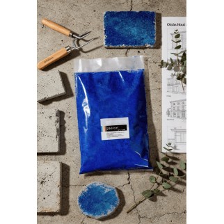 Poudre pigment bleu outremer pour béton ciré dans sachet transparent, entourée d’outils et échantillons de béton.