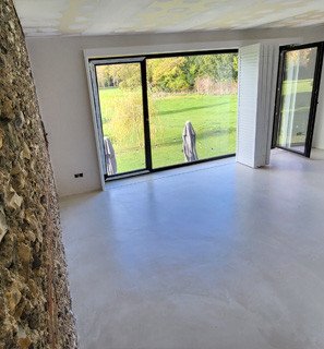 Salon lumineux avec mur blanc et grandes fenêtres donnant sur jardin verdoyant; intérieur prêt à être peint en couleur mur cuisine blanche.